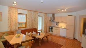 A cozy living room with a wooden dining table, a sofa, and a kitchen area with white cabinets and appliances. - Bavaria Modern Family Stay (Prackenbach)