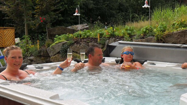 A hot tub with three people, surrounded by greenery and rocks. - Bavaria Modern Family Stay (Prackenbach)