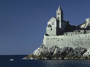 A historic stone castle with a prominent tower, situated on a rocky coastline with the sea in the foreground.