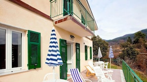 A balcony with white lounge chairs, green shutters, and striped umbrellas.