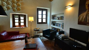 A cozy living room with a red leather sofa, a wooden coffee table, a bookshelf, a television, and a floor lamp. - Rustic Tuscan Cottage (Fivizzano)