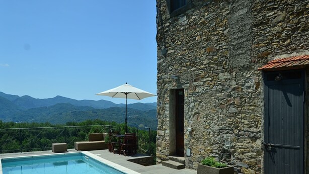 A stone building with a pool, outdoor furniture, and a view of mountains. - Rustic Tuscan Cottage (Fivizzano)
