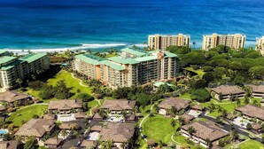A resort with multiple buildings, including high-rise hotels and bungalow-style accommodations, surrounded by lush greenery and a beachfront.