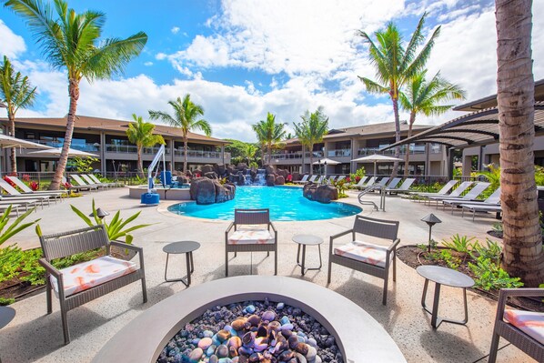 A pool area with lounge chairs, a fire pit, and palm trees.