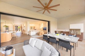 A modern kitchen with a built-in grill, dining area with a table set for four, and a cozy living room with a sofa and chairs. - K L V R Welcomes you to 4 Luana Garden Villas Building 11 in Oceanfront Resort (Lahaina)