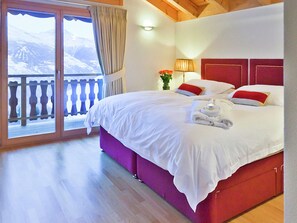 Une chambre d’hôtel avec un grand lit, un balcon offrant une vue sur les montagnes et un plafond en bois.