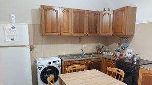 A compact kitchen with wooden cabinets, a built-in washing machine, a sink, and a dining table with chairs. - Lovely Holiday Home in Giardini Naxos near Sea (Taormina)