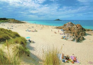 Ein Strand mit badenden Personen, einem Felsen und Booten im Wasser.