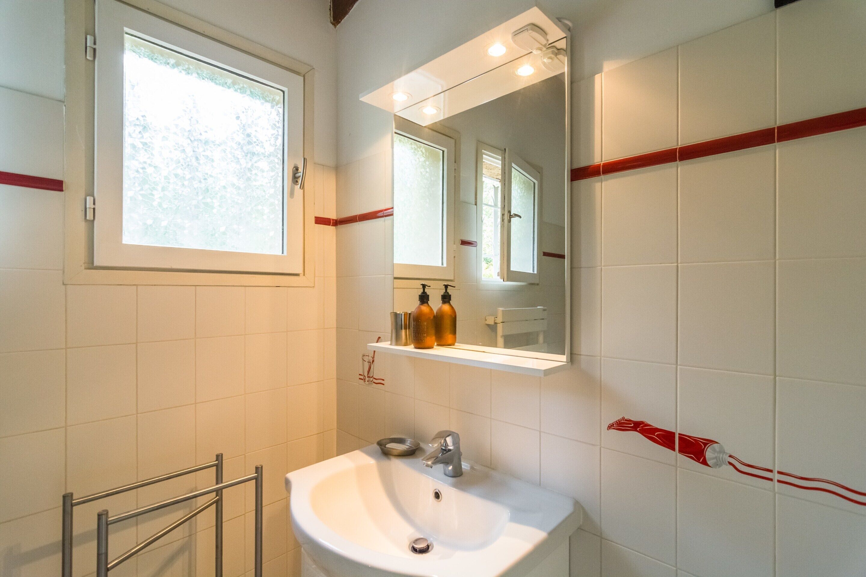 A bathroom with a white sink, a mirror, and a window.