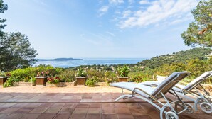 Eine Terrasse mit zwei Liegestühlen, gefliestem Boden und Blick auf das Meer und die Hügel.