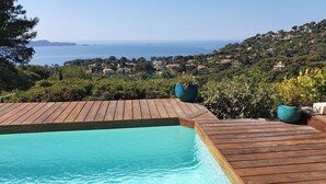 Eine Holzterrasse mit Schwimmbad, mit Blick auf eine Küstenlandschaft mit Häusern und Grünflächen.