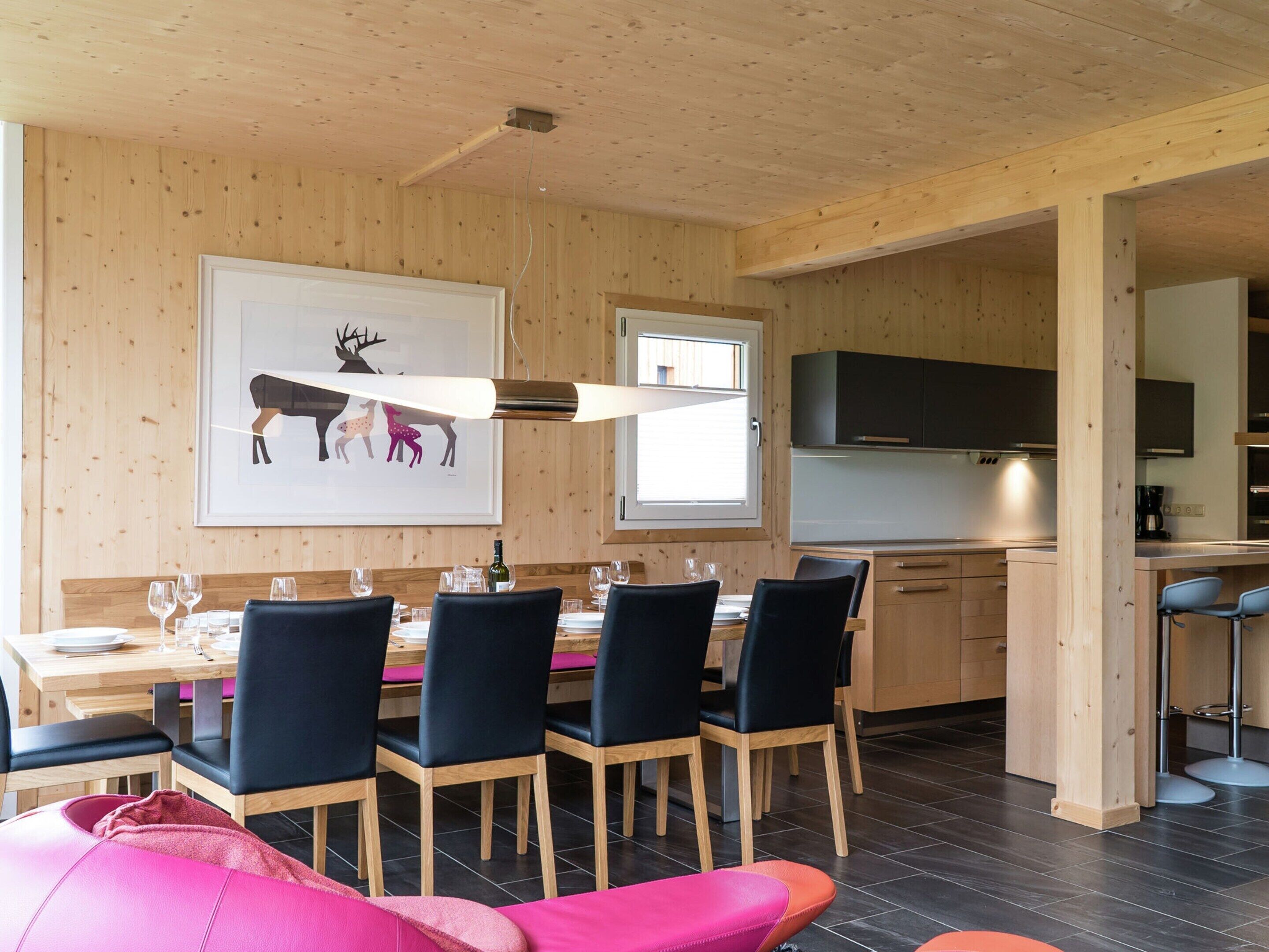 A modern dining area with a wooden ceiling, a dining table set for four, and a kitchen area with wooden cabinets and a black countertop.