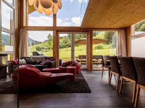 A spacious living area with a red sofa, a wooden ceiling, and large windows offering a view of a green landscape. - Modern Chalet in Sankt Georgen ob Murau With Sauna (Sankt Georgen am Kreischberg)