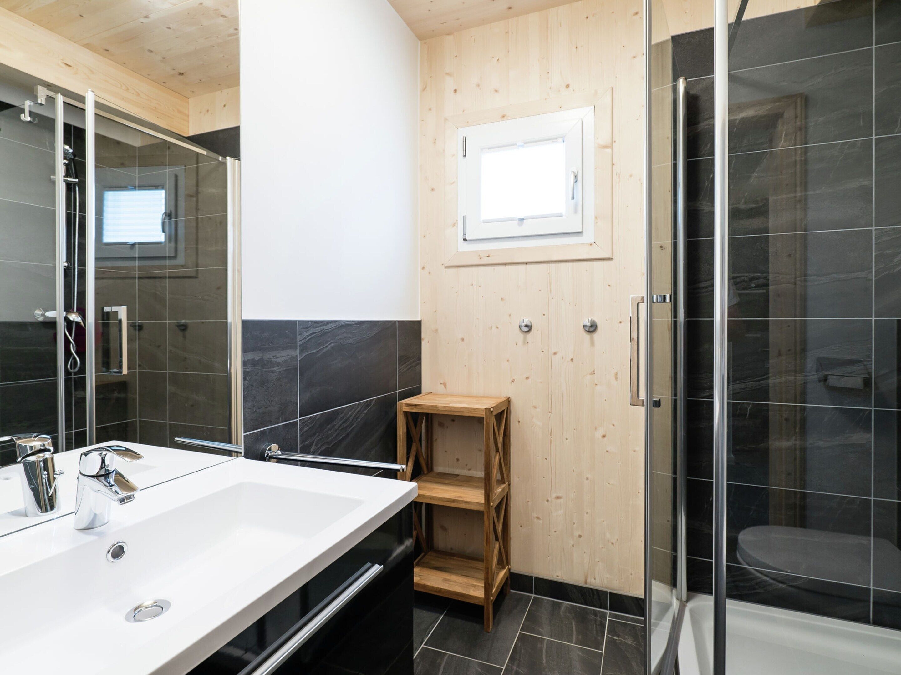 A modern bathroom with a large white sink, a glass-enclosed shower, and a wooden shelf unit.