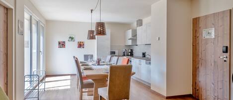 A modern kitchen with white cabinets, a dining area with a wooden table and chairs, and a large window providing natural light.