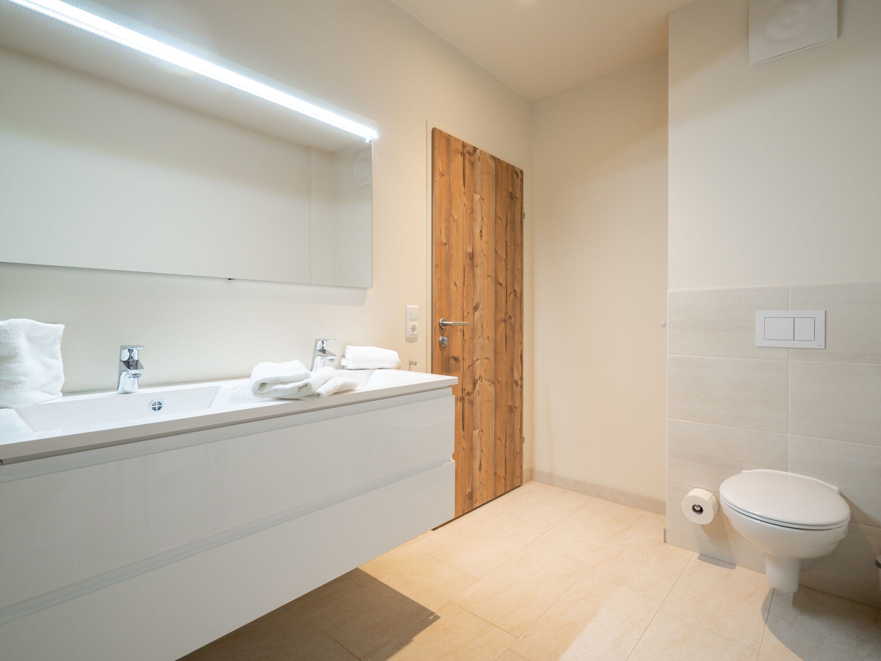 A modern bathroom with a large white sink, a wooden door, and a toilet.