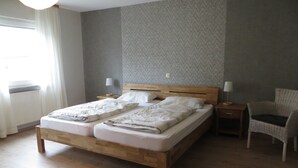 A double bed with a wooden frame, two bedside tables with lamps, a wicker chair, and a window with curtains. - Spacious Holiday Home in Haserich near Lake (Haserich)