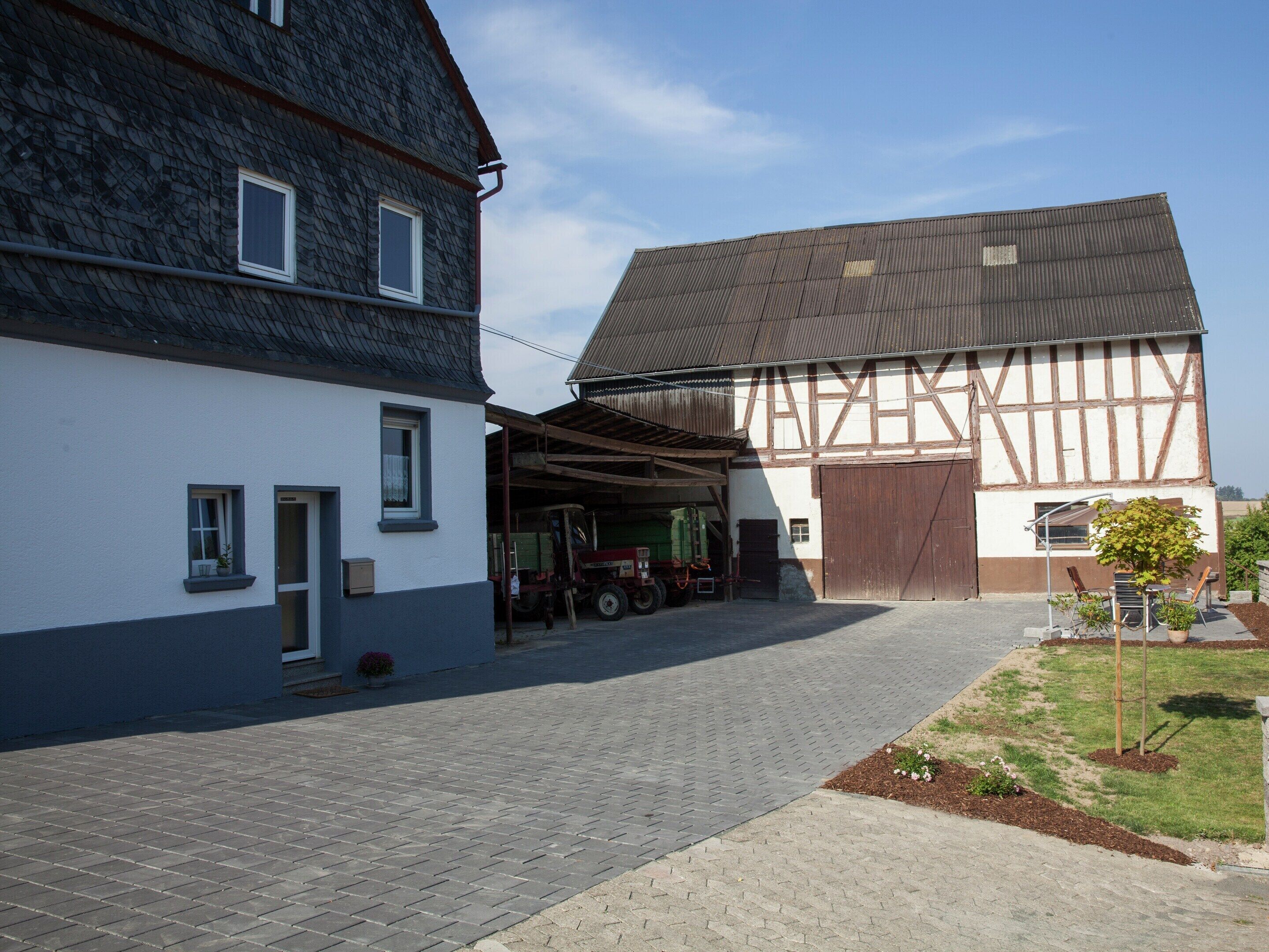 A building with a large garage door, a covered driveway, and a small garden area with a tree and flowers.