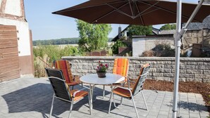 An outdoor patio with a table and chairs, a large umbrella, and a stone wall. - Spacious Holiday Home in Haserich near Lake (Haserich)