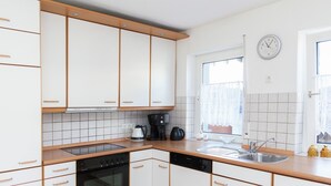 A modern kitchen with white cabinets, a black oven, a coffee maker, and a sink. - Spacious Holiday Home in Haserich near Lake (Haserich)