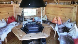 A cozy cabin interior with a central wood-burning stove, wooden walls, and fur-covered seating. - Apartment in Sonnen Near Ski Lifts (Sonnen)
