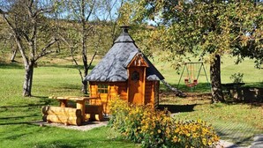 A wooden cabin with a sloped roof, a wooden bench, and a picnic table in a grassy area with trees and flowers. - Apartment in Sonnen Near Ski Lifts (Sonnen)