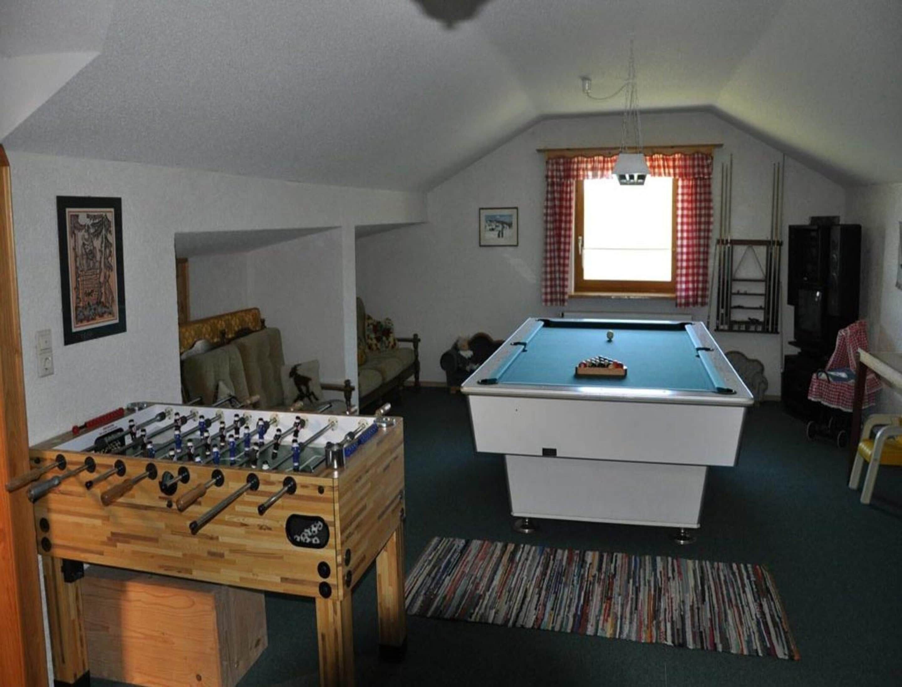 Une pièce avec une table de baby-foot, une table de billard, un canapé et une fenêtre avec des rideaux.