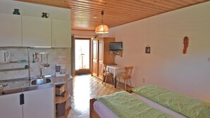 A compact room with a kitchenette, a bed with green patterned bedding, a wooden ceiling, and a television on a small table. - Apartment in Sonnen Near Ski Lifts (Sonnen)