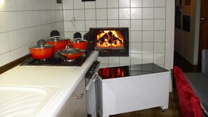 Una cocina con paredes de azulejos blancos, una estufa con ollas, un horno pequeño y un reloj en la pared.