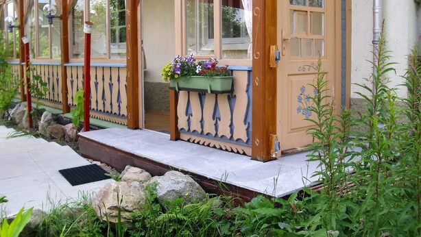 Una casa de madera con un porche, una puerta con un número y una ventana con macetas de flores.