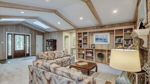 Ein geräumiges Wohnzimmer mit einer großen Couch, einem Couchtisch und einem Bücherregal, das mit Büchern und Dekorationsgegenständen gefüllt ist.