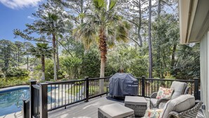 Eine überdachte Terrasse im Freien mit Korbmöbeln, einem Grill und einem Pool.