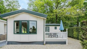 Eine kleine, eingeschossige Holzhütte mit weissen Wänden und grünem Zierstreifen, einer Veranda mit weissem Geländer und einem blauen Sonnenschirm.