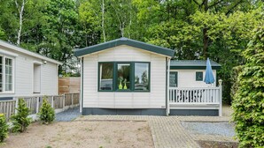 Ein kleines, eingeschossiges Mobilheim mit umzäunter Terrasse und gepflasterter Auffahrt.
