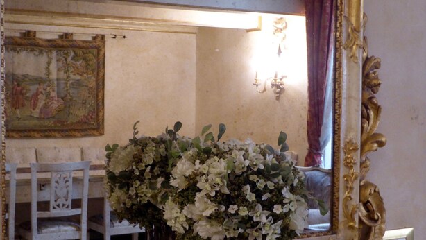 A mirror with a gold ornate frame, a white chair, and a vase with white flowers. - Apartment in Florence Near Duomo (Florence)