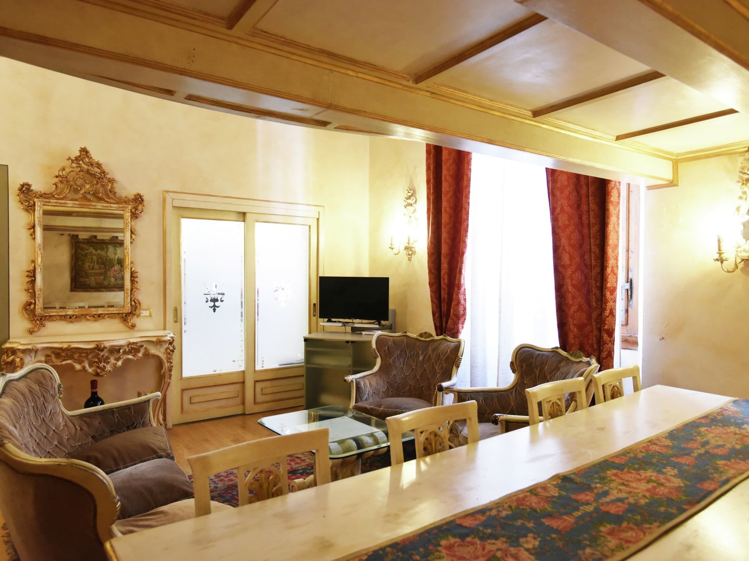 Un comedor con una mesa larga, varias sillas, un televisor y un espejo decorativo.