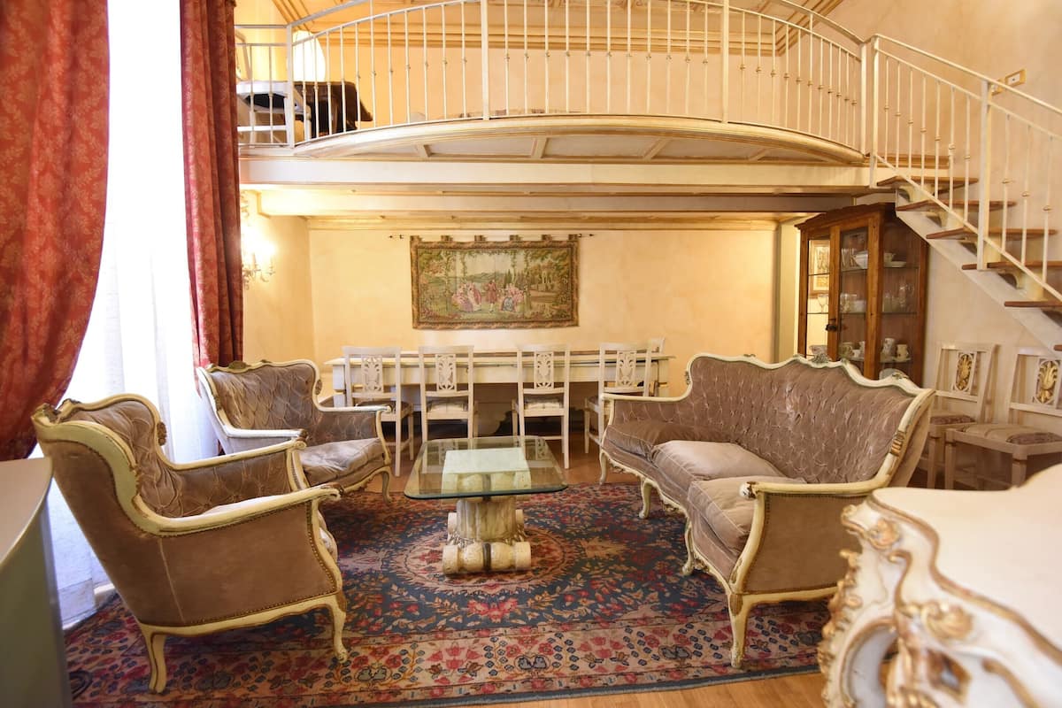 Amplia sala de estar con techo alto, una escalera curva y un comedor con muebles antiguos.