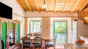 Une cuisine avec des meubles de rangement en bois, une table à manger avec des chaises, un réfrigérateur et une fenêtre donnant sur un paysage verdoyant.