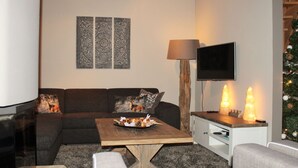 A modern living room with a sectional sofa, a coffee table, a flat-screen TV, decorative wall art, and a Christmas tree. - Chalet in Lungau With Sauna and hot tub (Sankt Margarethen im Lungau)