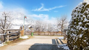 A snow-covered parking area with a wooden fence, a green trash bin, and a mountain in the background. - Chalet in Lungau With Sauna and hot tub (Sankt Margarethen im Lungau)