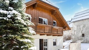 A two-story wooden chalet with a balcony, a covered patio, and a snow-covered tree. - Chalet in Lungau With Sauna and hot tub (Sankt Margarethen im Lungau)