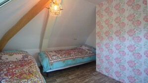 Ein kleiner, gemütlicher Raum mit schräge Decke, einem Einzelbett mit gemustertem Überwurf, einem kleinen Nachttisch und floraler Tapete an einer Wand.