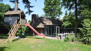 A rustic cabin with a thatched roof, a wooden slide, and a glass-enclosed porch area.