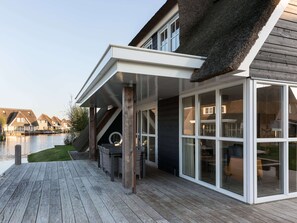 A modern house with a wooden deck, large glass windows, and a thatched roof.