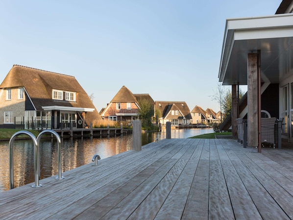 A wooden deck leading to a canal with thatched-roof houses.