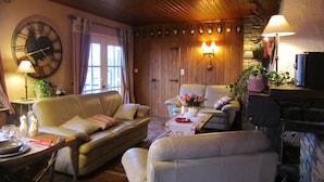 Un salon chaleureux avec un plafond en bois, une grande horloge murale, un canapé, une table basse et un téléviseur.