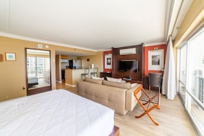 Quarto de hotel com uma cama grande, um sofá, uma TV e vista para a cidade.