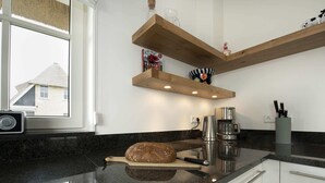 A kitchen with a granite countertop, a loaf of bread, a coffee maker, and wooden shelves above the counter. - Chic Villa With a Fireplace at Tjeukemeer (Delfstrahuizen)