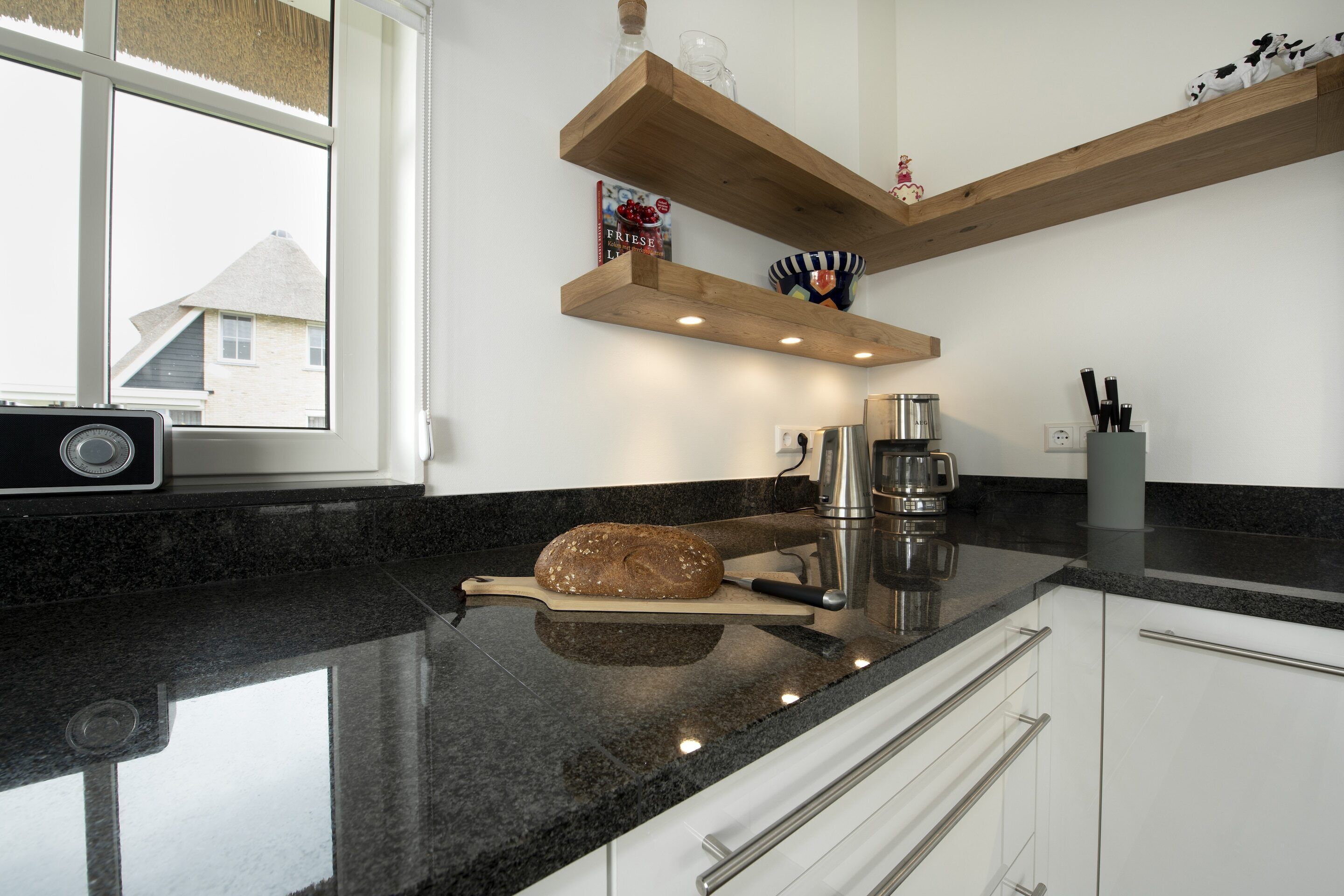 Una cucina con un piano di lavoro in granito, una pagnotta su un tagliere, una macchina per il caffè e mensole in legno sopra il bancone.