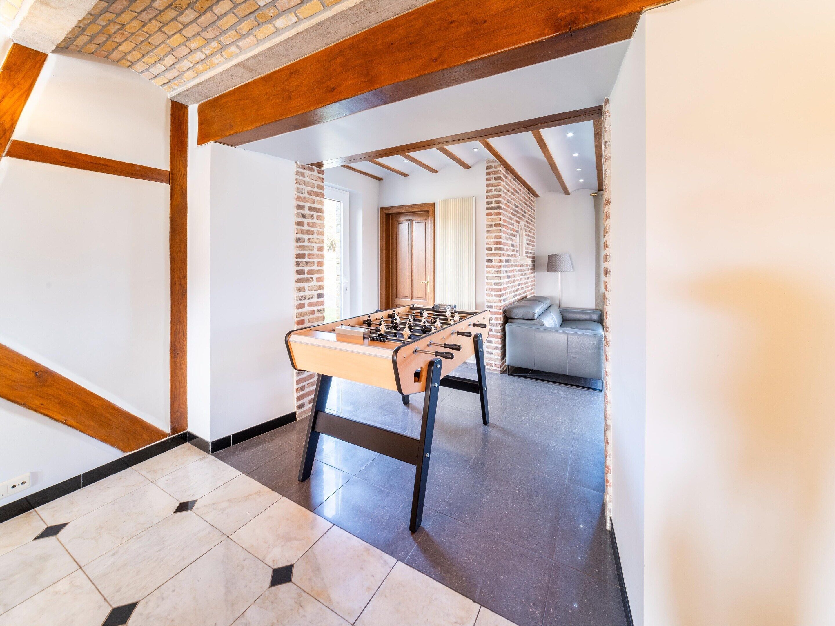 A room with a foosball table, a grey sofa, and a brick wall.